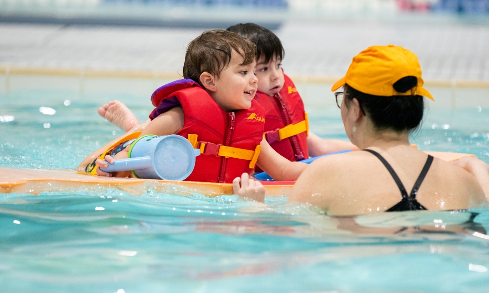 Two students enjoy a mat ride in a swimming lesson at Winskill.