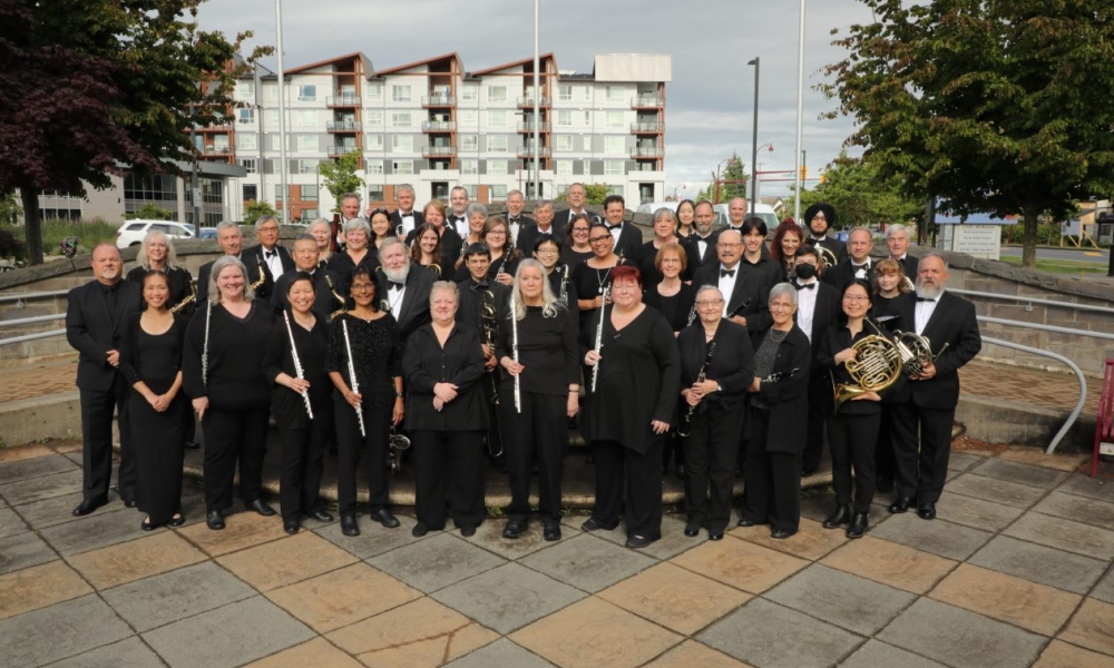 Delta Concert Band, in all black, stand in front of the steps of Social Heart Plaza. 