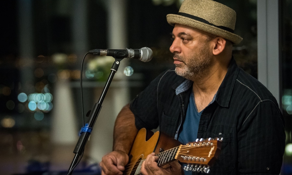 Ranj Singh performs on stage with his acoustic guitar in hand. 