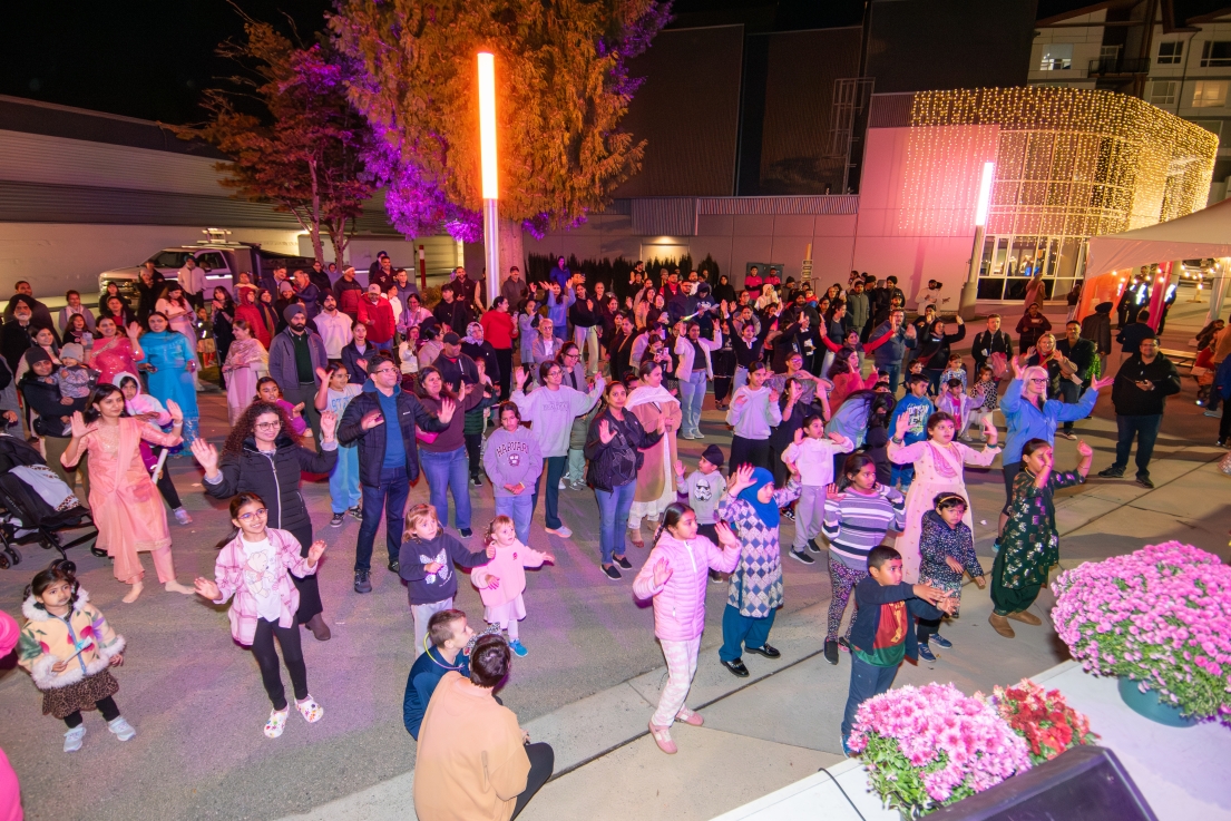 Crowd of attendees dancing and following along to an interactive performance at DIYAfest, with families gathered in a brightly lit outdoor event space at night.