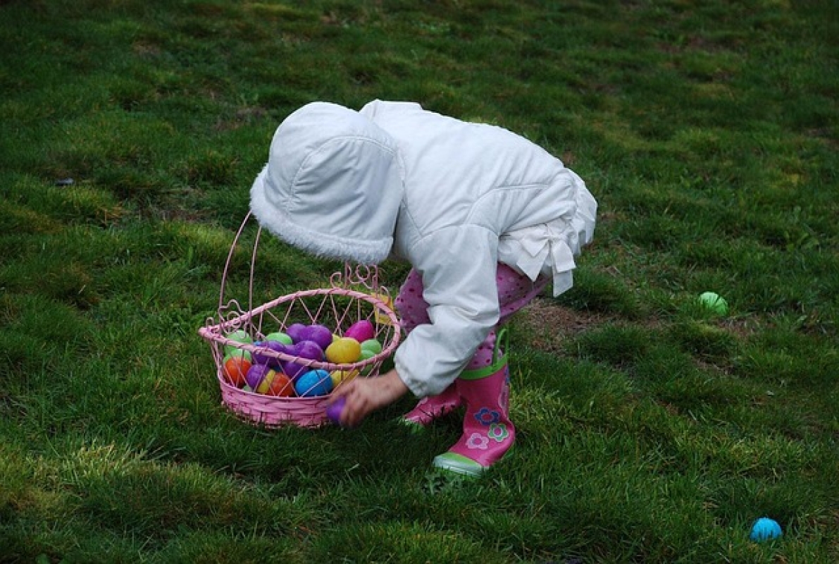 A child picks up colourful Easter Eggs on the grass. 