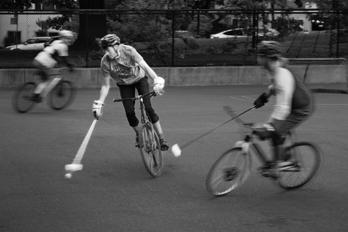 Blurry with motion, three bike polo players compete for a loose ball with their mallets. 