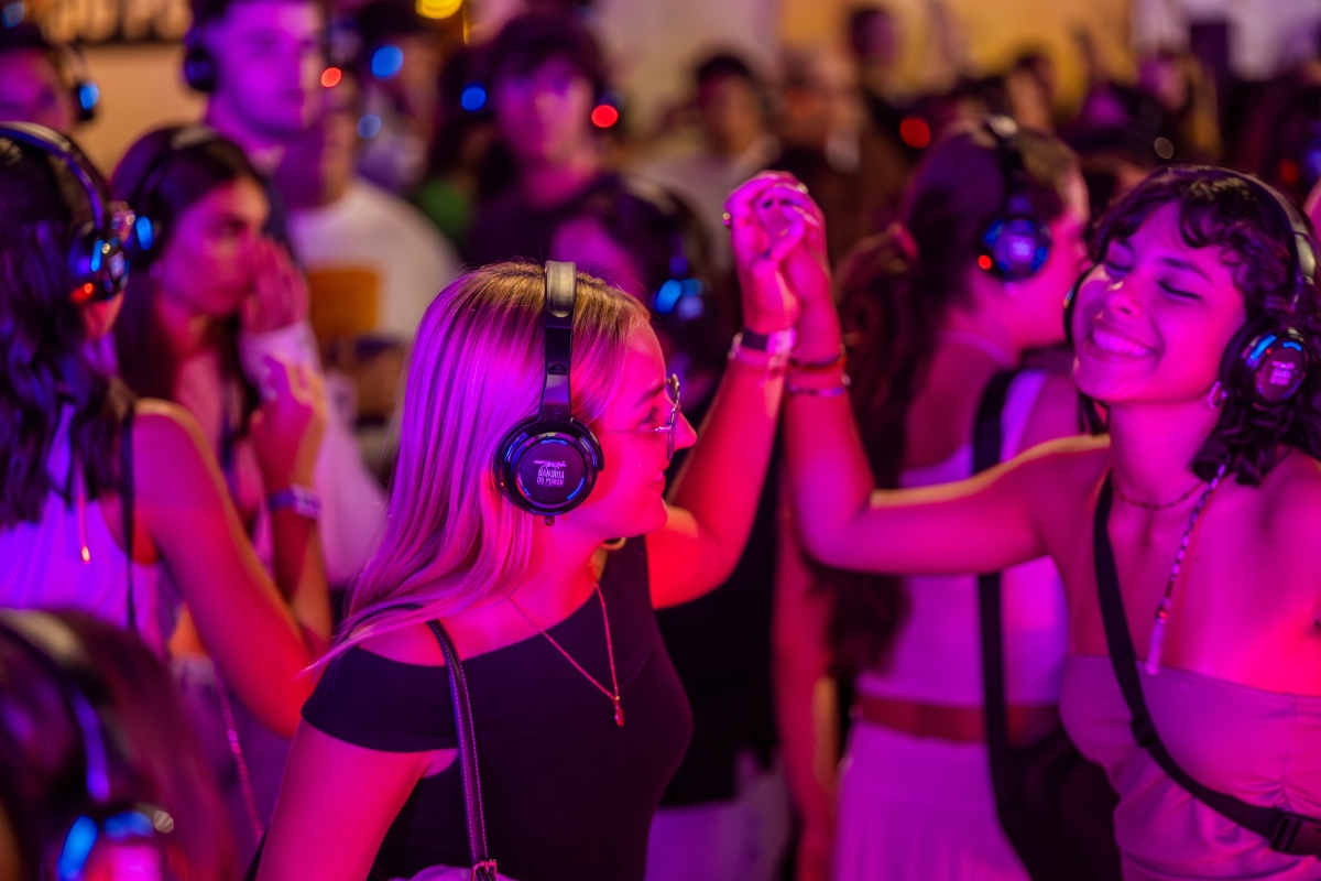 two girls dance in a crowd with headphones on at the silent disco dance party.