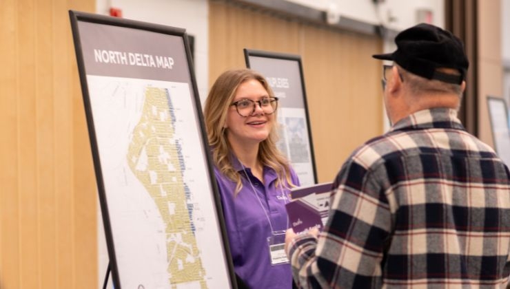 Delta staff member standing next to a map of North Delta and speaking with a member of the public at the PLAN-A-THON event.