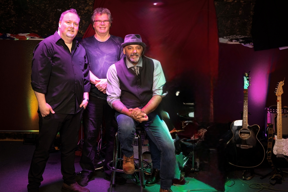 The three members of Ranj Singh Trio promotional photo on stage in a club. 