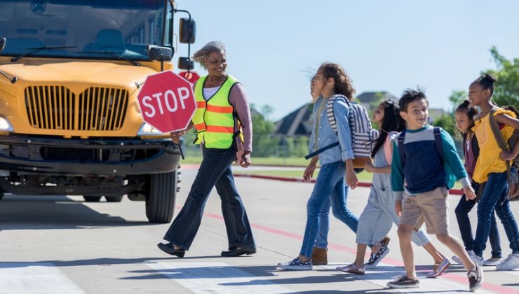Crossing guard holding stop sign leading students through a crosswalk.