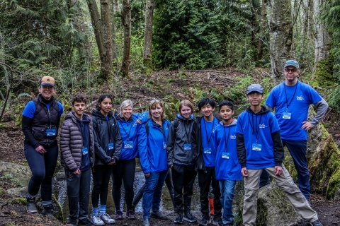 A group of people wearing blue jackets standing in the woods. 