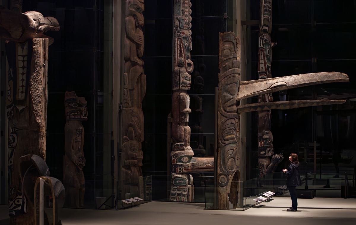 A woman stands in front an enormous totem pole at the Museum of Anthropology.